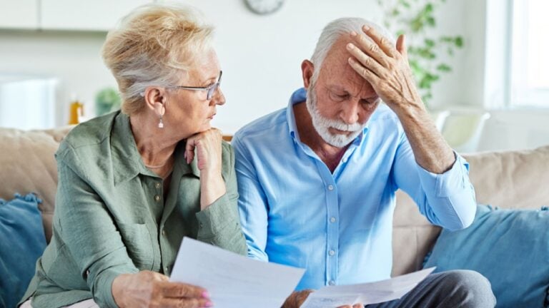 Senior couple checking bills and calculating expenses using a calculator at home, debt taxes and home budget concept, worried married elderly couple