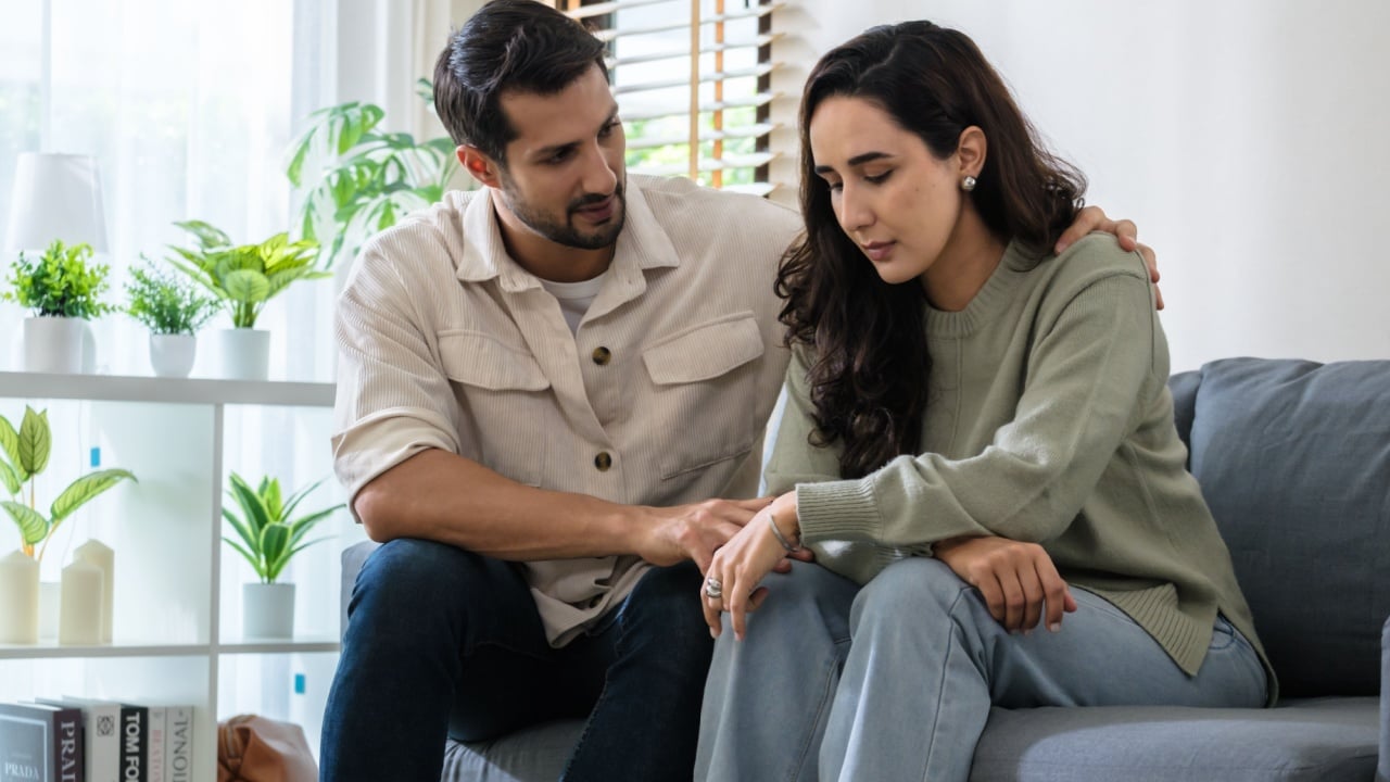 Supportive couple in emotional moment at home as woman struggles with sadness and stress, expressing