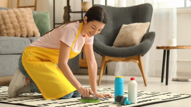 Young housewife cleaning carpet in living room
