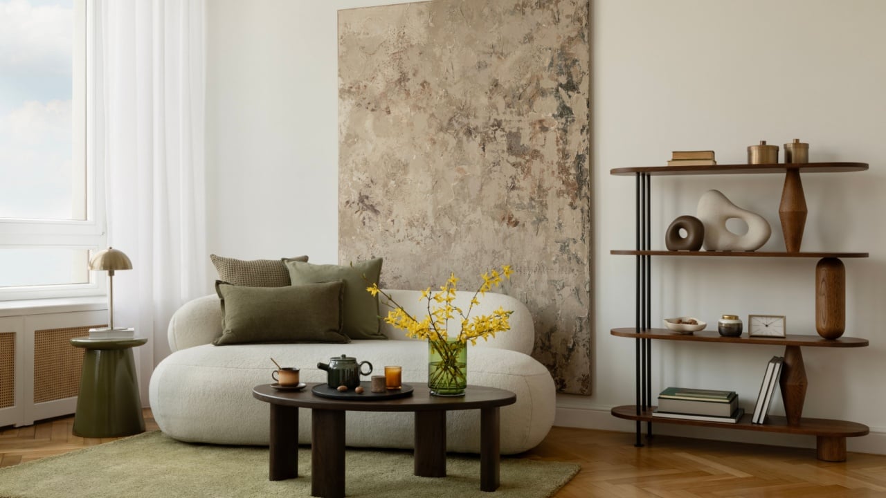 Minimalist living room with green-toned art, sculptural lamp, cozy white sofa, and a round coffee table with warm-toned decor and eucalyptus branches.