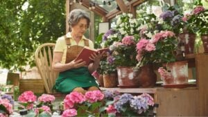 A graceful senior woman reads a book in her vibrant garden filled with colorful flowers and plants.
