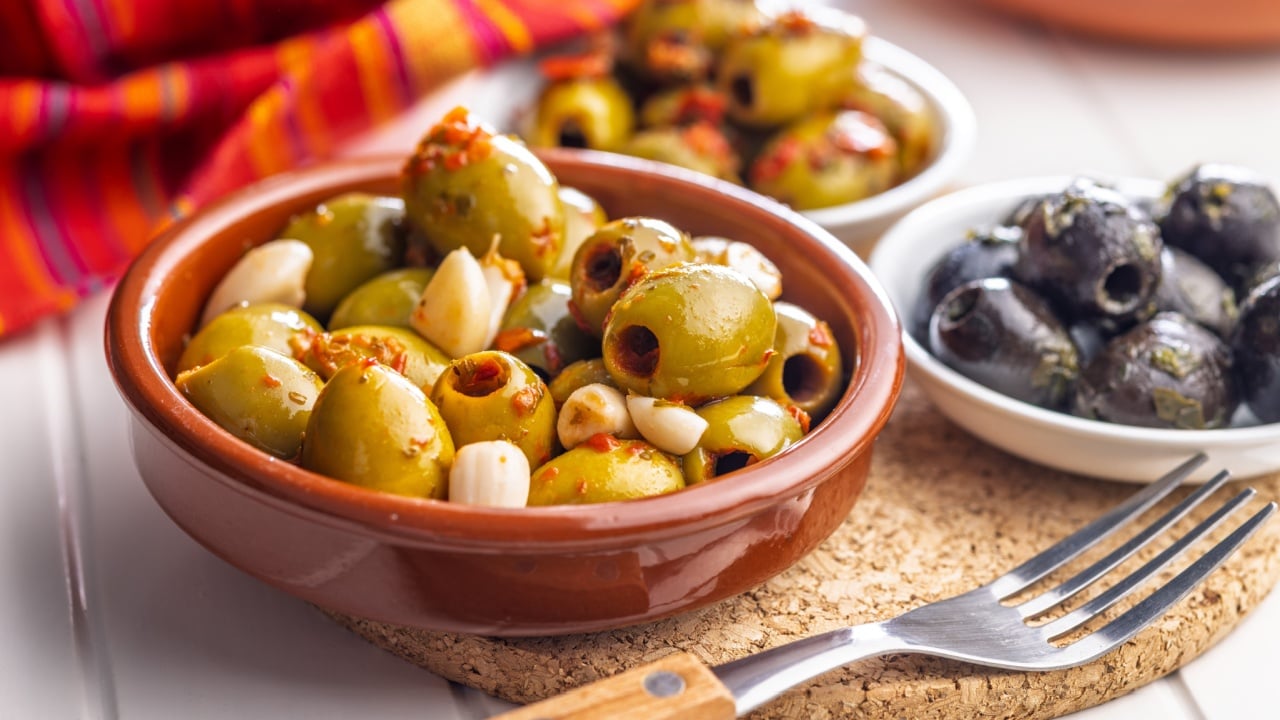 Tapas. Flavored pickled olives in bowl on a white table.