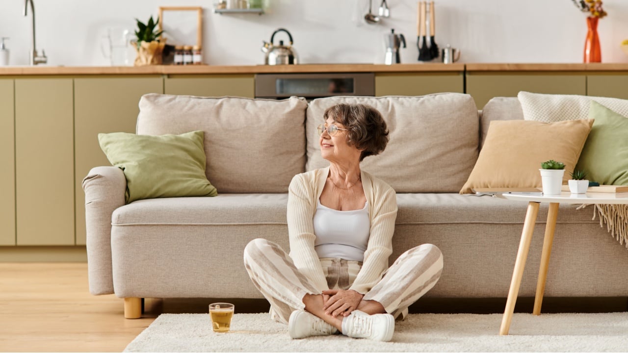 Senior woman sits comfortably on the floor in her cozy home, enjoying a peaceful moment.