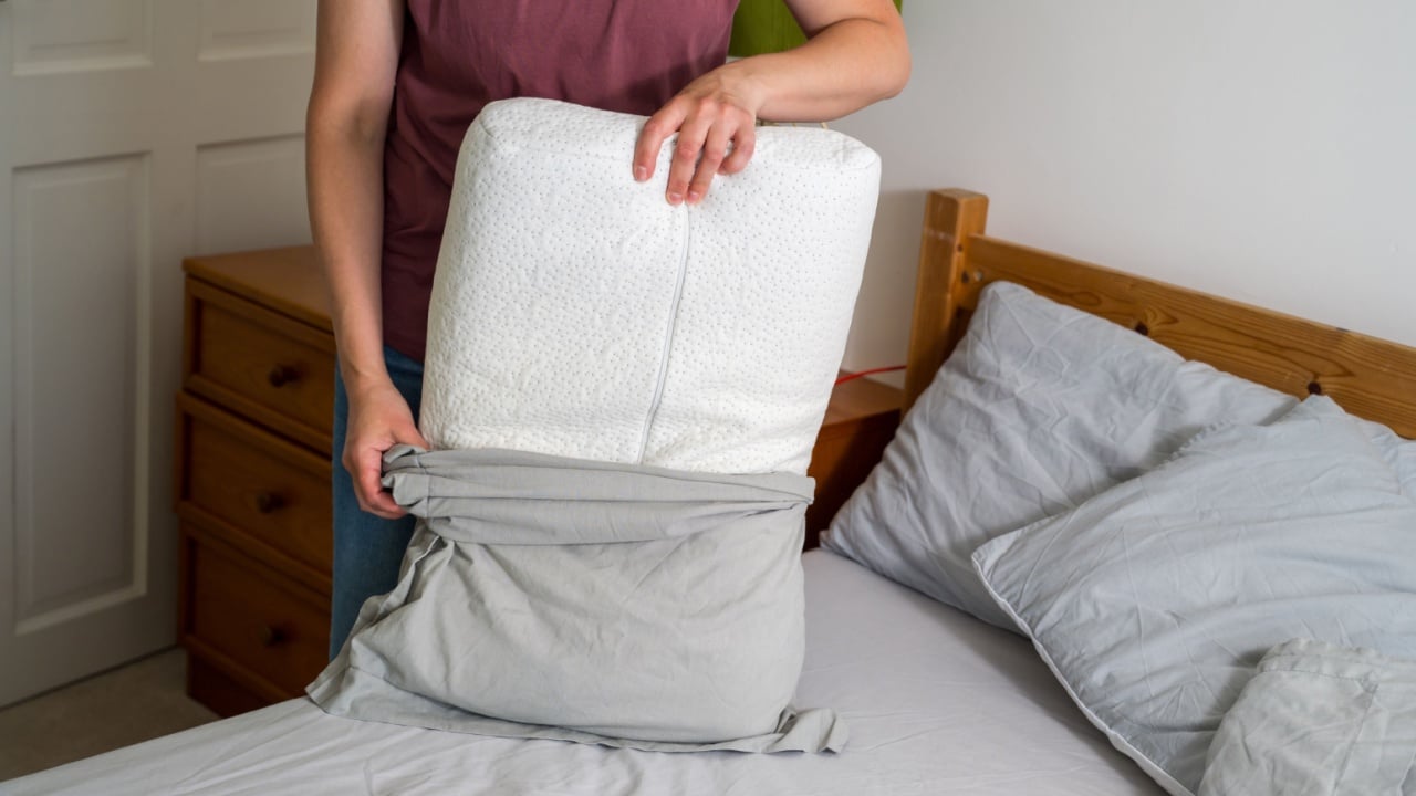 Woman changing pillow case with fresh clean grey cotton bed sheets
