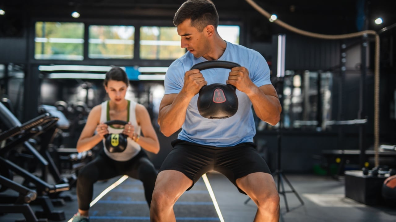 Personal coach do kettle bell squat exercise with client at gym. Athletic couple doing kettle bell goblet squat exercise during cross training in gym