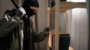 Thief searching money in the books with flashlight foreign house.