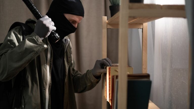 Thief searching money in the books with flashlight foreign house.