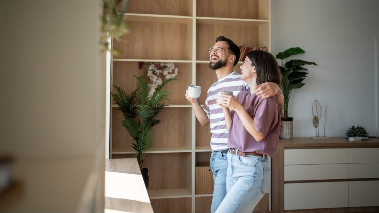 Young couple laughing and enjoying a cup of coffee together in their modern, light-filled apartment, embracing the start of a new day with happiness and love