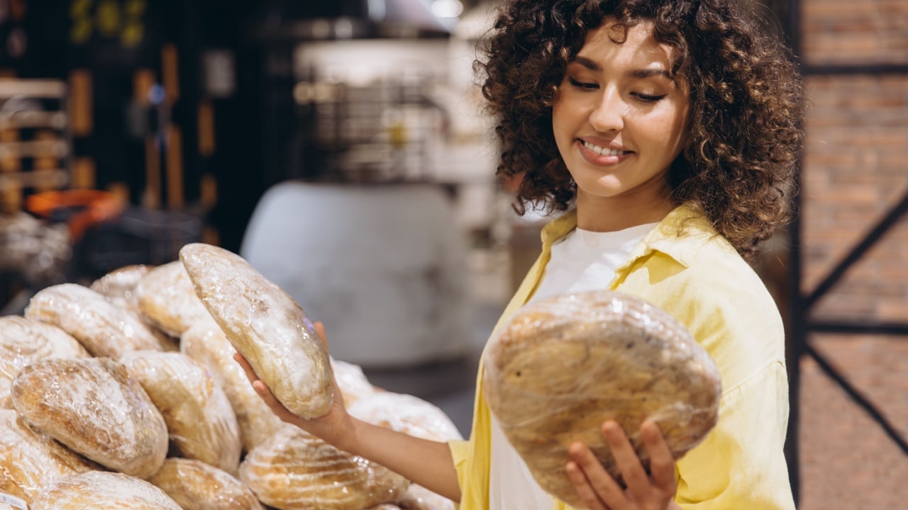 Smiling woman comparing two loaves of packaged bread while shopping in the supermarket bakery, enjoying the selection of fresh baked goods