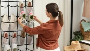 Woman putting sneakers into organizer at home. Shoe storage