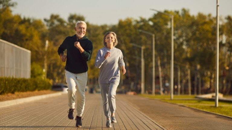 Happy retired couple jogging together. Healthy smiling senior husband and wife in sportswear running along city street during outdoor fitness workout on sunny summer morning. Sport, old age concept