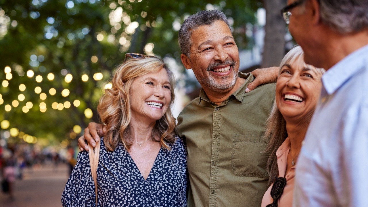 Group of happy senior friends sharing a moment outdoor while embrace. Older men and laughing women chatting together during a walk. Close up face of cheerful retirees enjoying in a lively city street.