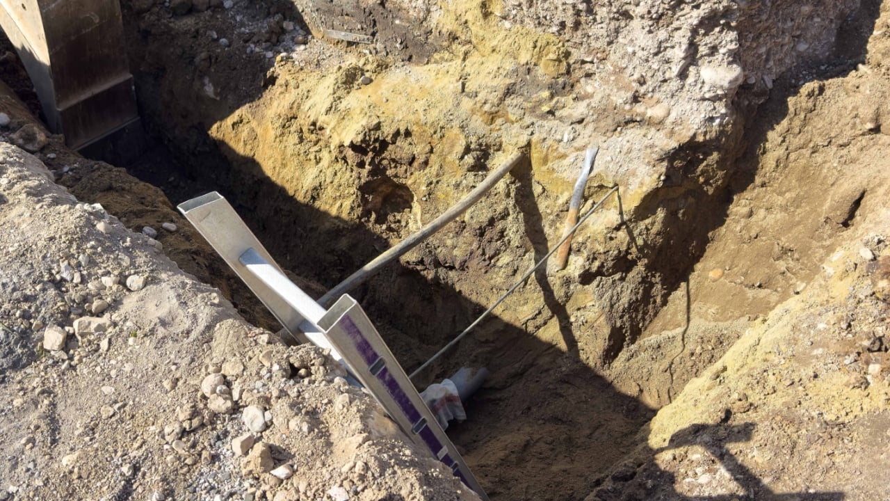 Trench construction excavation showing soil layers and tools in sunlight.