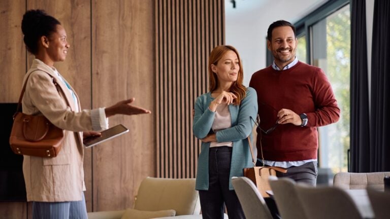 Happy couple looking at a house for sale with their real estate agent. Copy space.