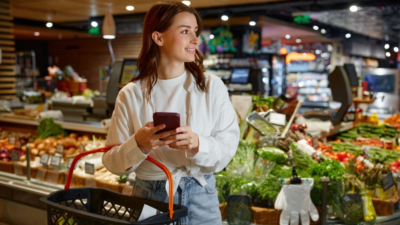 A woman is shopping in a grocery store while looking at her phone