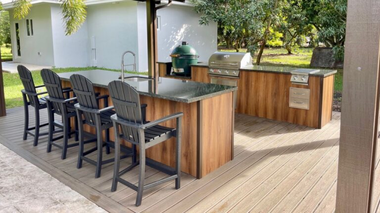 A stylish modern outdoor kitchen featuring wooden cabinetry, stainless steel grill, granite countertop, and bar seating on a backyard patio, designed for outdoor cooking and entertainment.