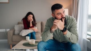 Man feeling sad and upset, sitting silently while woman is in the background. Relationship problems and emotional distance