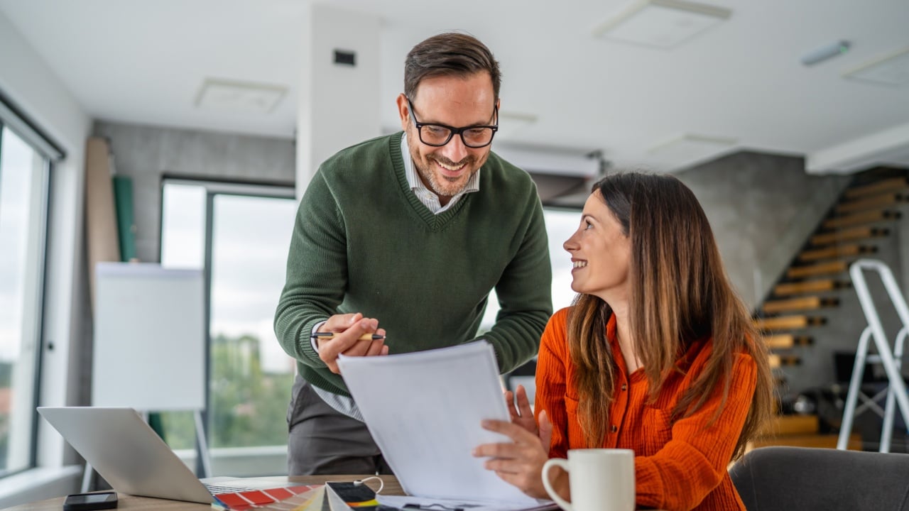 Young couple reviews documents and color swatches on a laptop while planning their home renovation, budgeting and making design decisions together for a new living space