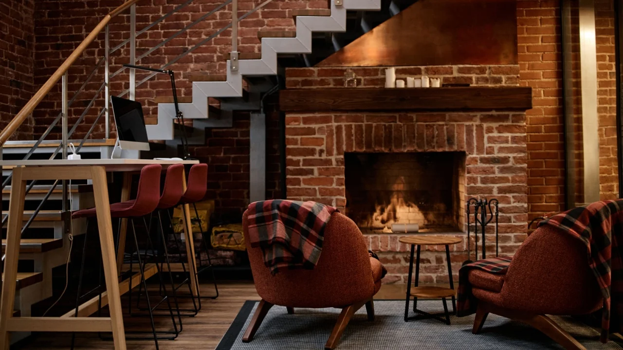 Modern business office interior featuring empty seating area with mid century style chairs and barstools arranged near brick fireplace and staircase, no people visible