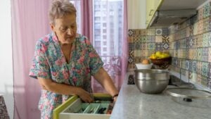An elderly woman is preparing food in the kitchen at home. Senior people cooking. Take cutlery out of the kitchen drawer, step 2