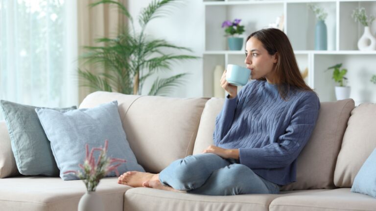 Relaxed woman in blue drinking coffee or tea sitting on a couch at home