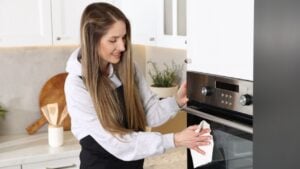 Woman wiping oven with paper towel in kitchen