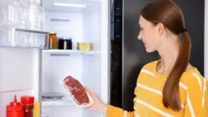 Woman taking raw beef meat from refrigerator in kitchen