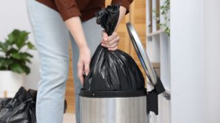 Woman taking out plastic bag with garbage from trash bin indoors, closeup