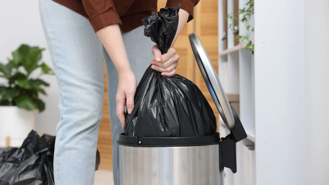 Woman taking out plastic bag with garbage from trash bin indoors, closeup