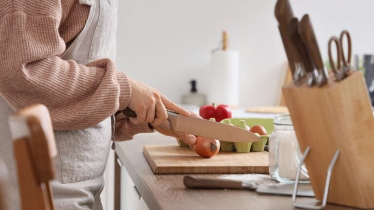 Woman cutting onion with knife at table in kitchen