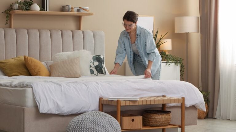Professional decorator making bed in stylish bedroom