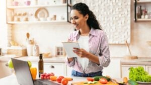 Woman Using Laptop While Preparing Meal in Kitchen During Daylight Hours