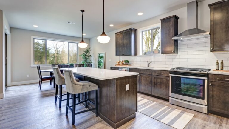 New kitchen boasts dark wood cabinets, white backsplash subway tile and over sized island with white and grey quartz counter illuminated by pendant lights. Northwest, USA