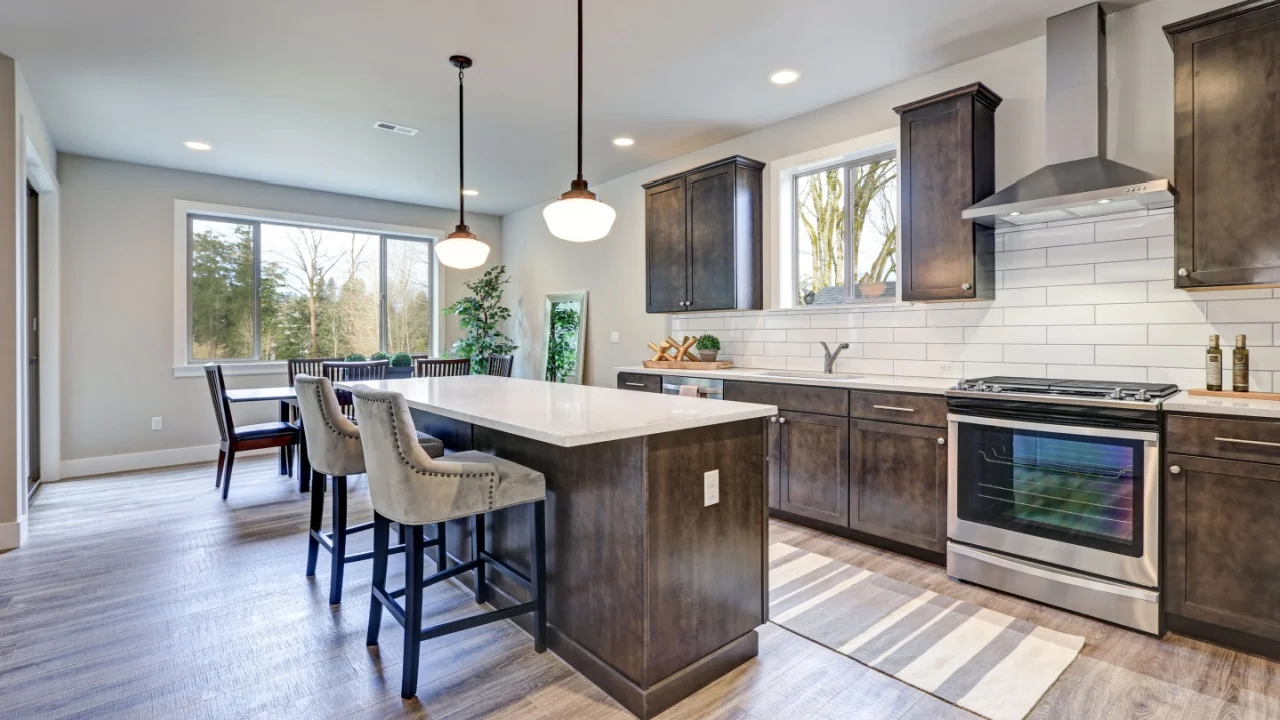 New kitchen boasts dark wood cabinets, white backsplash subway tile and over sized island with white and grey quartz counter illuminated by pendant lights. Northwest, USA