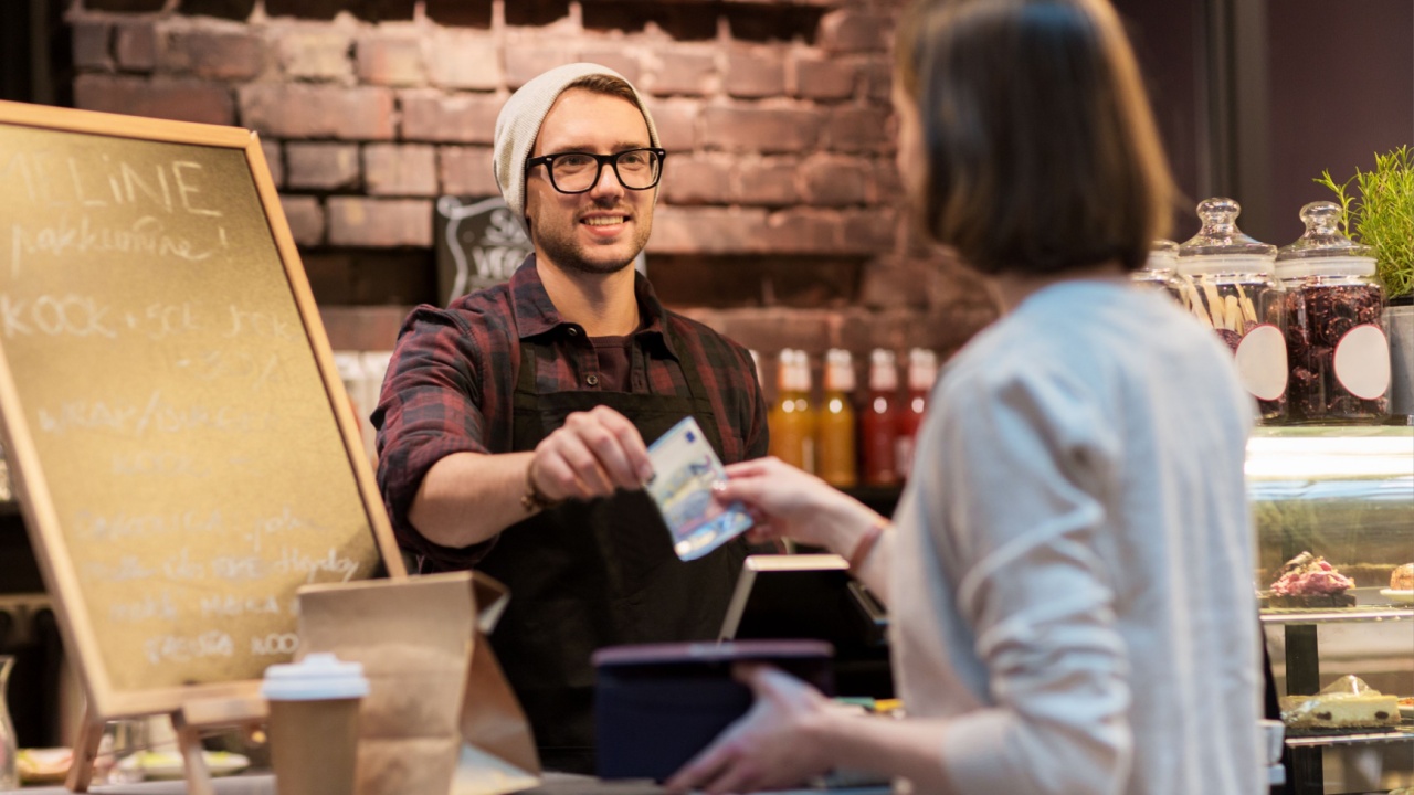 small business, payment, people and service concept - happy barman and woman paying money at cafe