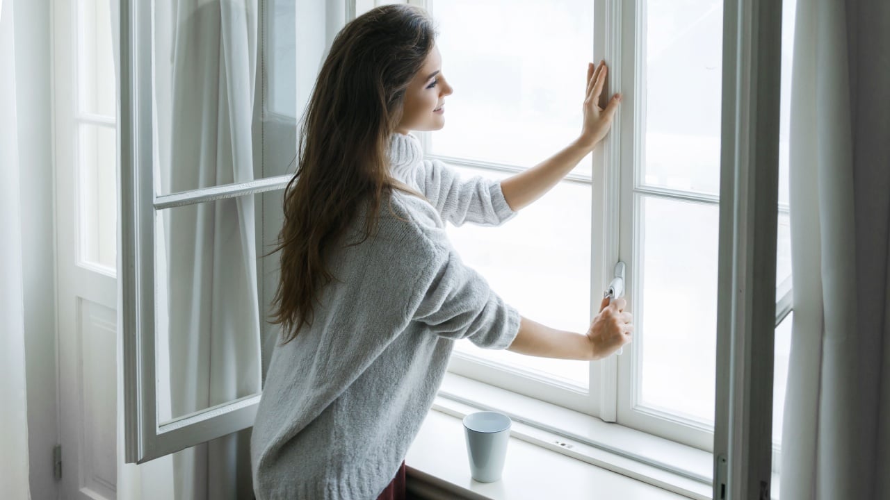 Woman is opening window to look at beautiful snowy landscape outside