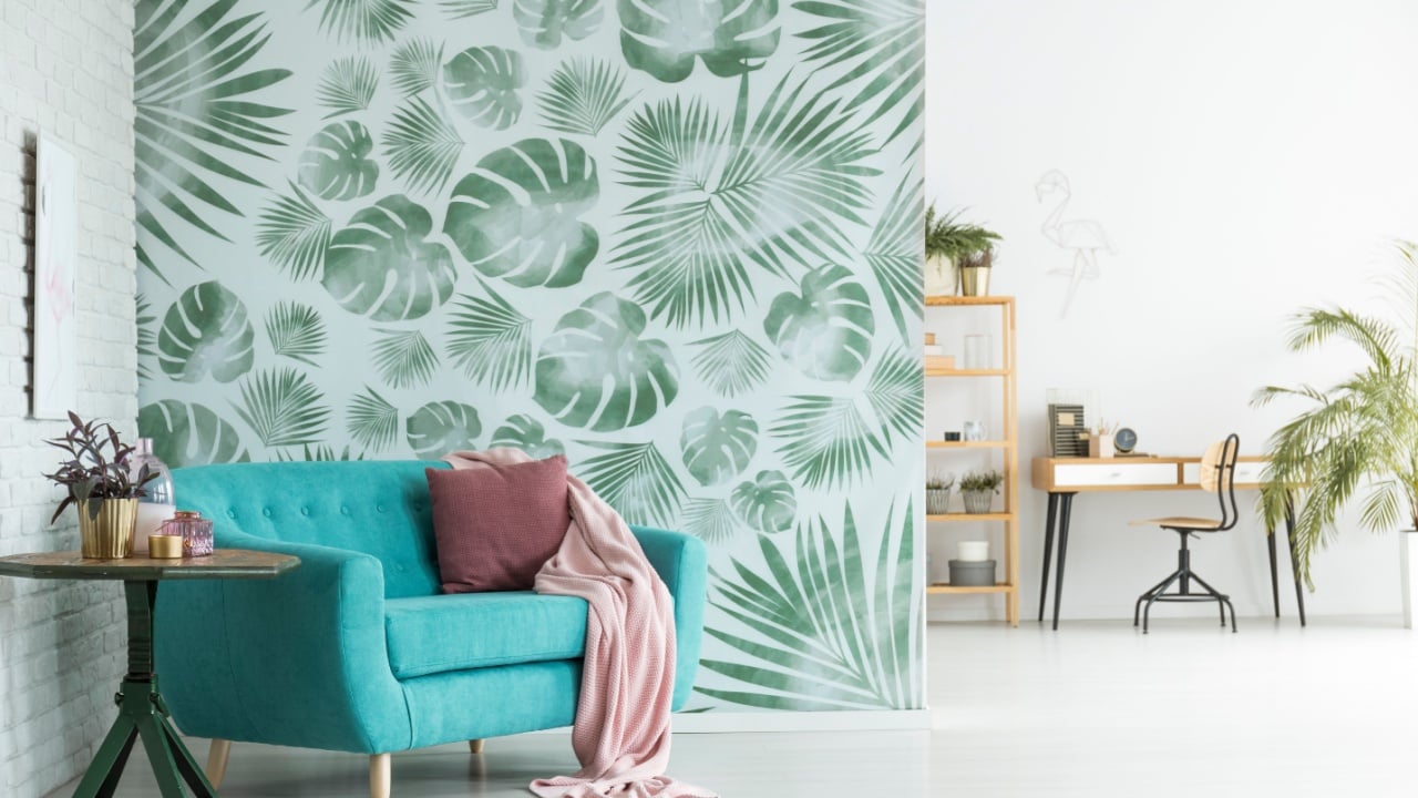 Pink blanket and pillow on blue settee next to a table with plant in room with workspace and floral wallpaper