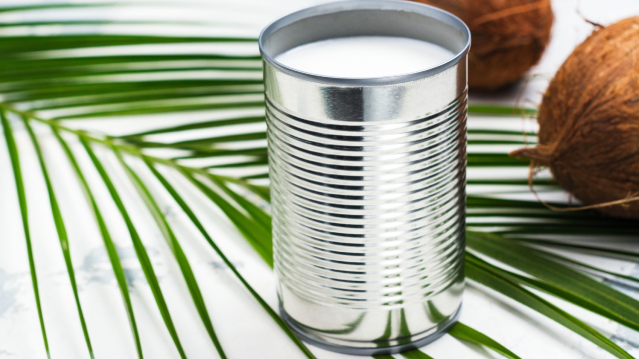Opened tin can with coconut milk drink. Alternative non dairy vegan milk on white stone table