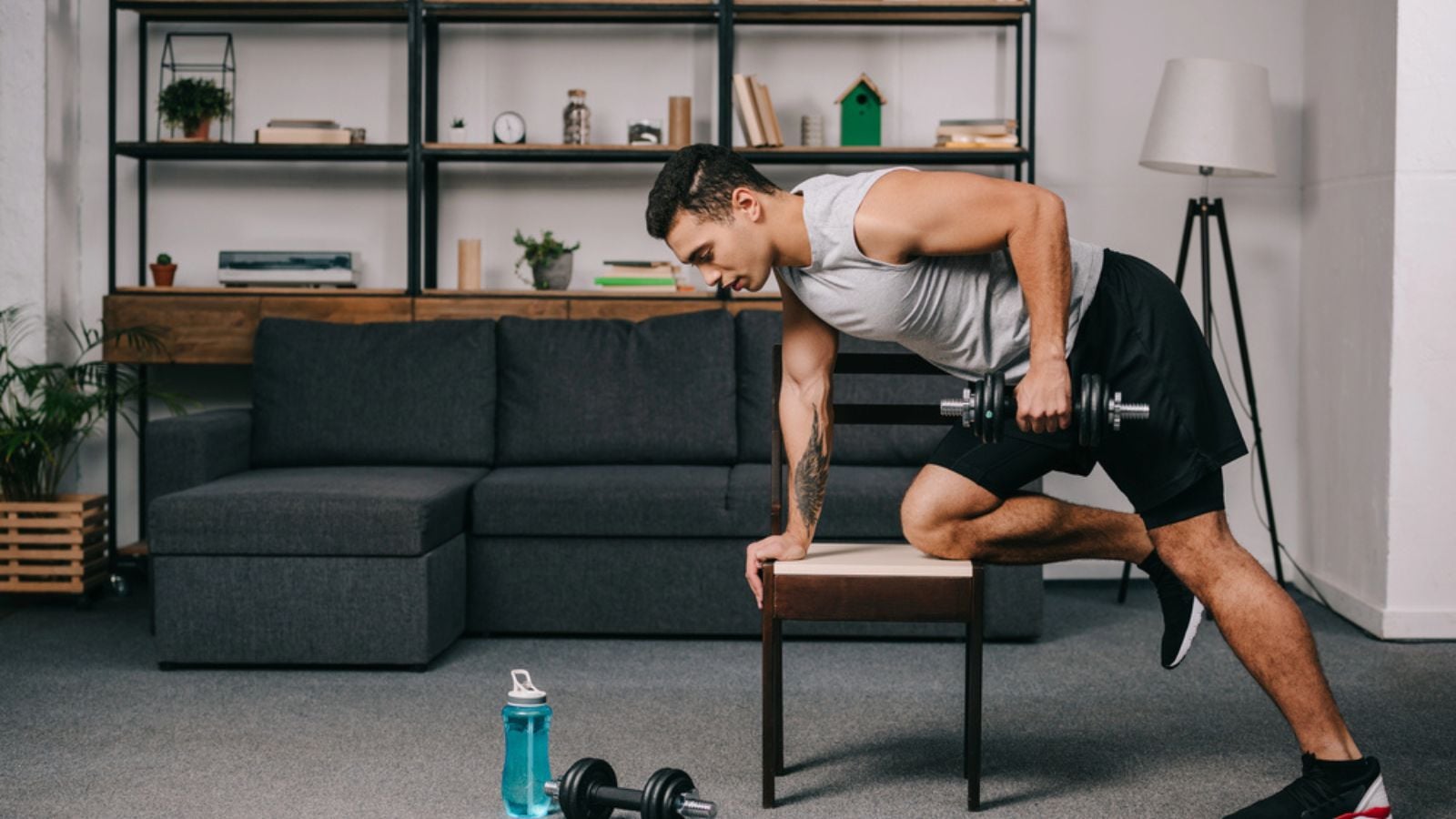 man doing exercise with dumbbell on chair in living room