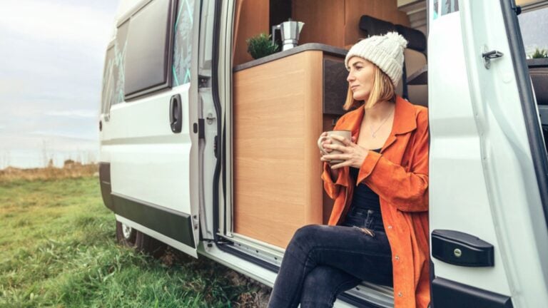Woman drinking coffee sitting at the door of a campervan