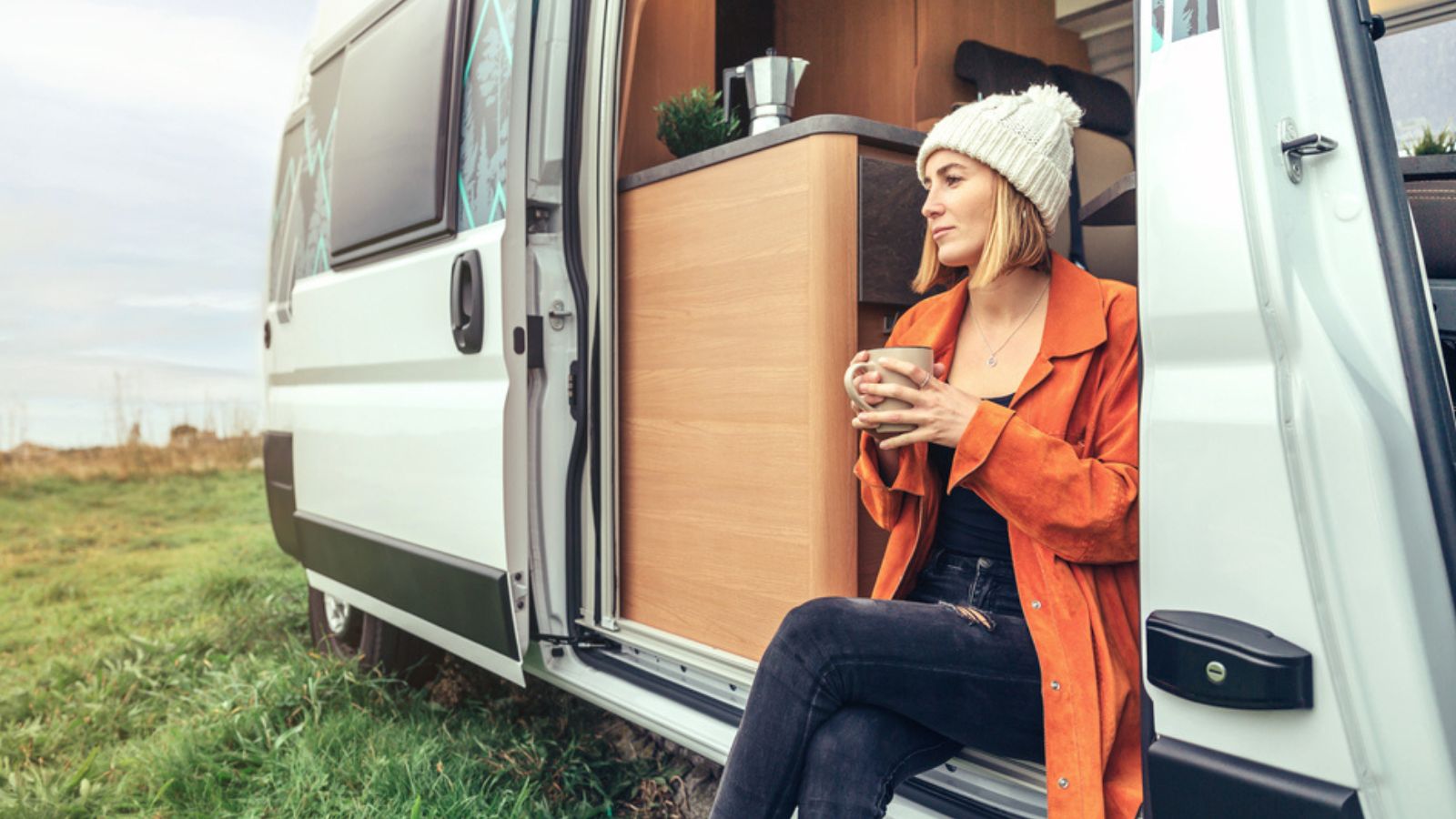 Woman drinking coffee sitting at the door of a campervan