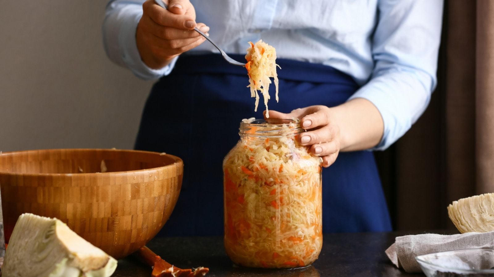 Woman putting tasty sauerkraut in glass jar on on table at kitchen, closeup