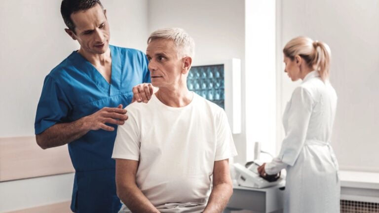Worried man wearing white shirt sitting on bed in medical room