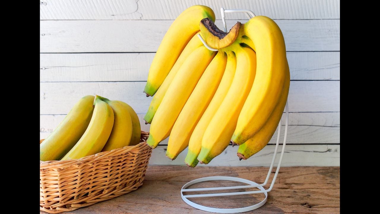 Yellow ripe banana hanging on hanger with white wooden background.