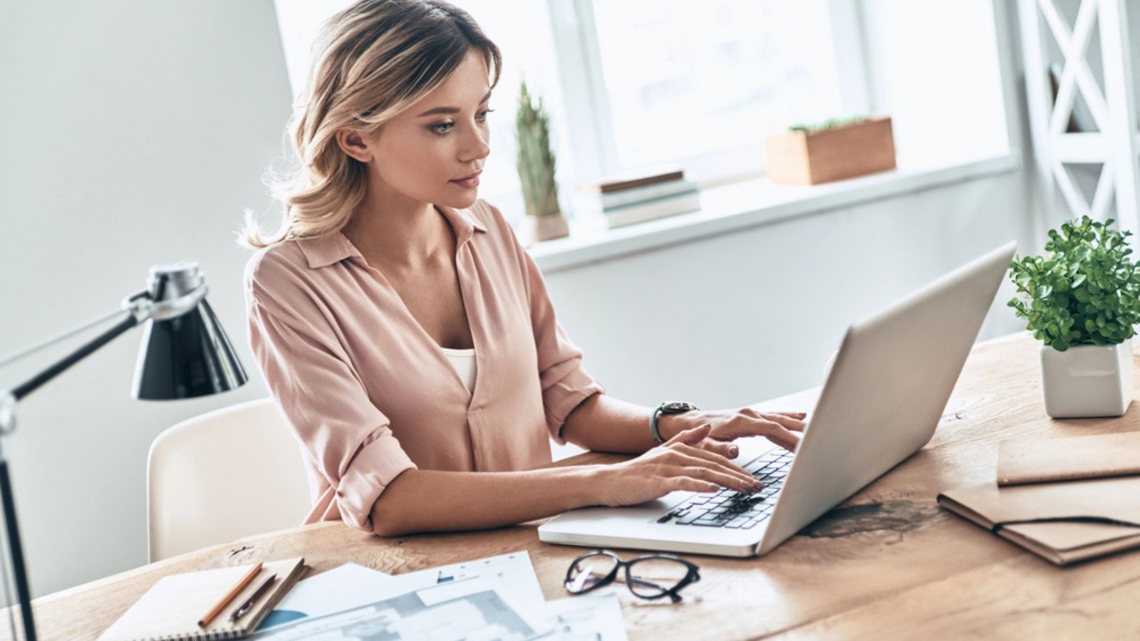 Young woman using laptop and sitting at table with papers documents