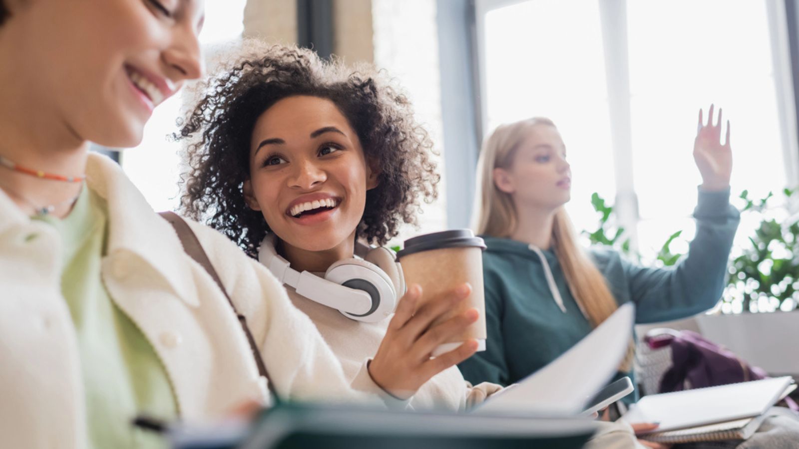 happy african american woman with headphones and coffee to go talking to blurred friend during lecture