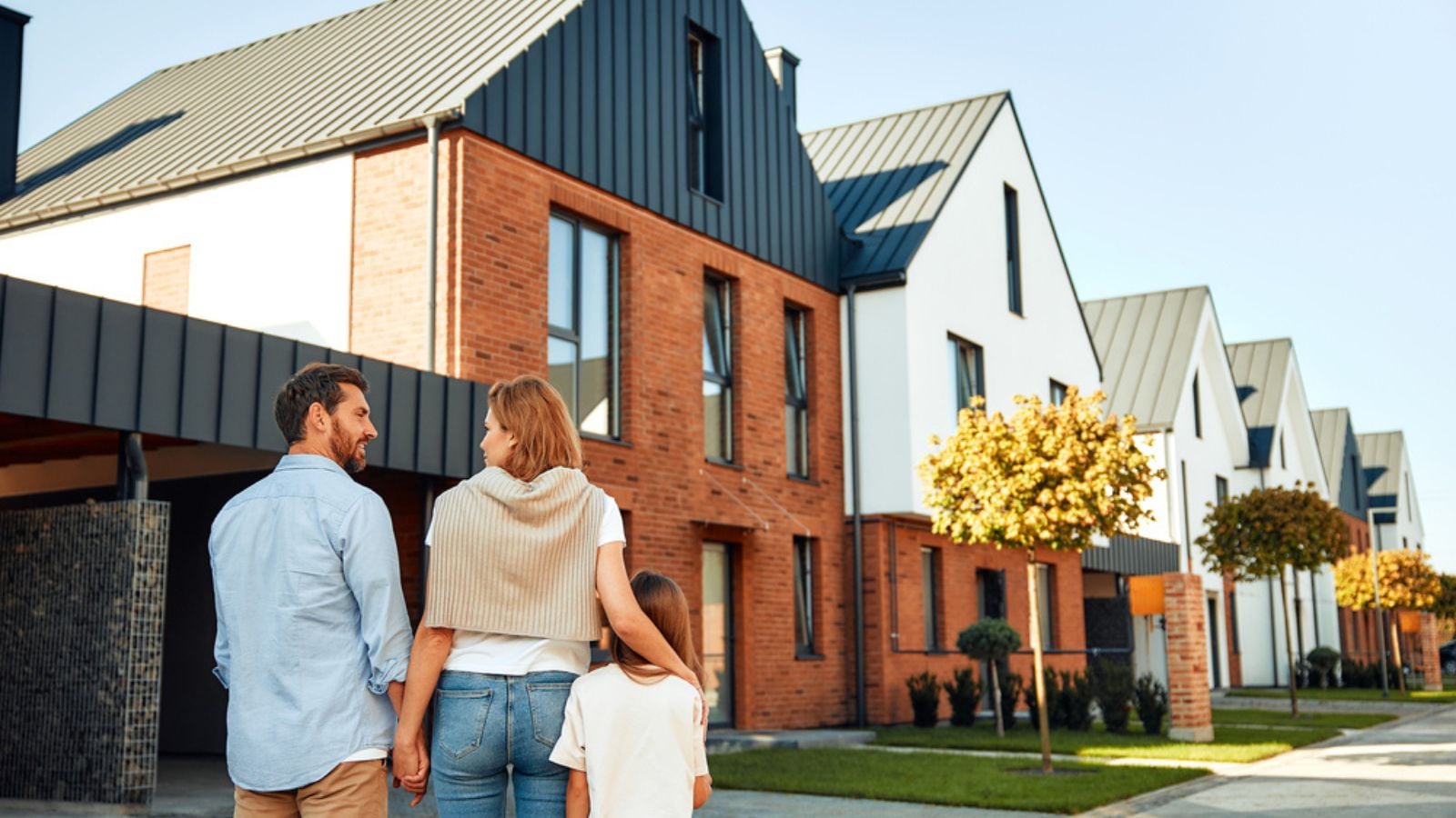 happy young family standing in front of new home buying a house