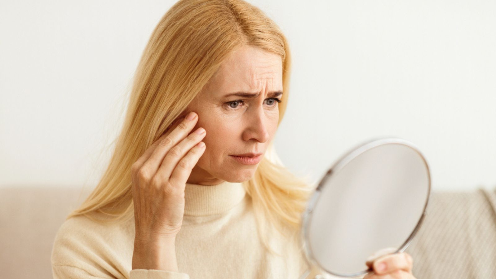 older woman looking in mirror at skin aging wrinkles worried stress