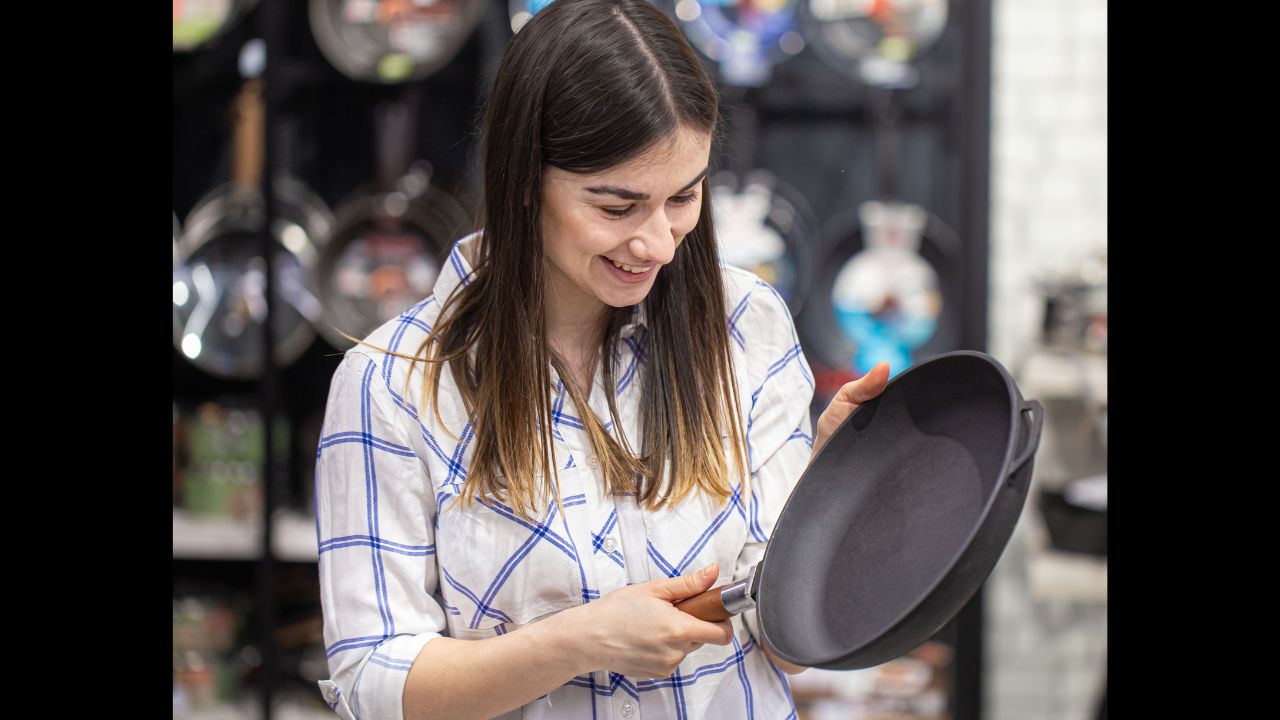 A young woman in the store chooses a frying pan . The concept of shopping for a home.
