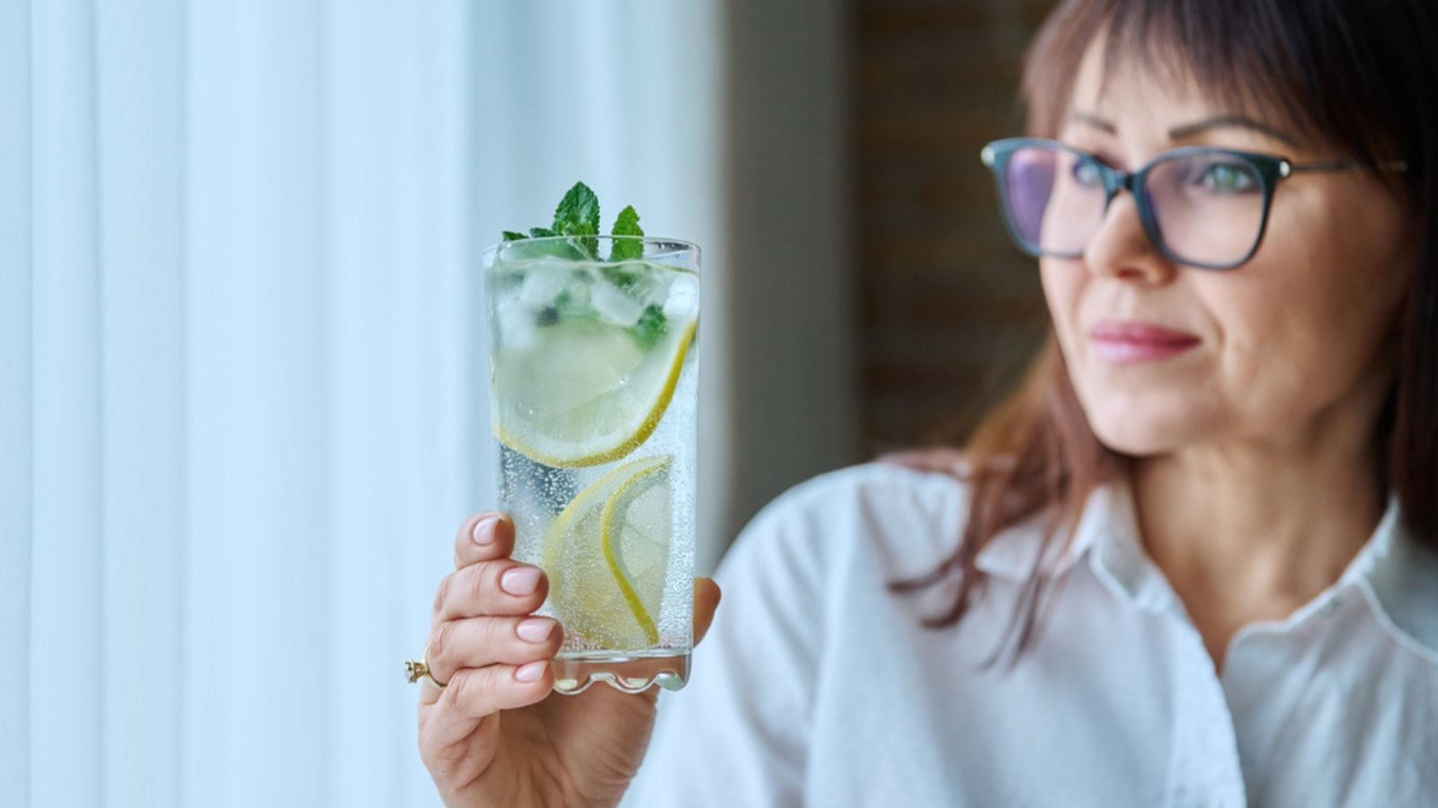 Cool fresh drink sparkling water with ice lemon mint leaves in womans hand. Summer healthy cold drinks, healthy lifestyle, proper nutrition, antioxidant, hot summer season concept